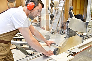 friendly carpenter with ear protectors and working clothes working on a saw in the workshop