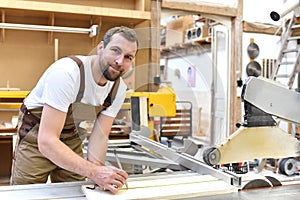 friendly carpenter with ear protectors and working clothes working on a saw in the workshop