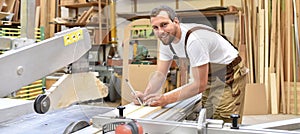 friendly carpenter with ear protectors and working clothes working on a saw in the workshop