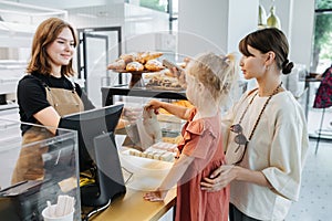 Friendly cashier handing pastry goods in a bag to mom with a daughter.