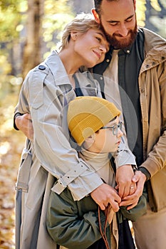 Friendly caucasian family with child hugging, in love, standing in park