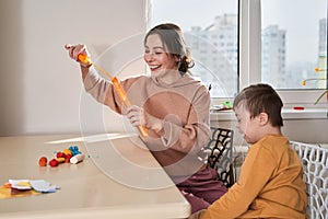 Friendly caucasian woman blowing soap bubbles with her son at the kitchen