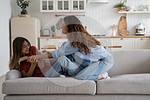Friendly Caucasian woman and teenage girl entertain themselves sits on sofa in spacious bright house
