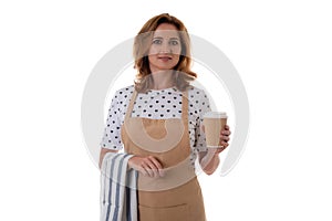 Friendly caucasian young woman in apron holding takeaway paper coffee cup and dishcloth towel, isolated in white background.