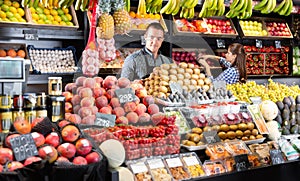 Friendly man and woman laying out vegetables and fruits in shop photo