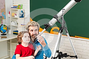 Friendly child in classroom near blackboard desk. Pupil watching stars with a teacher. Astronomy telescope.