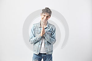 Friendly dark-haired guy dressed in a white t-shirt, jeans and a denim jacket stands on the white background in the