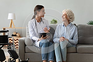 Friendly doctor consulting disabled woman, giving prescription at home