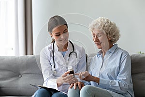 Friendly doctor consulting older woman patient, holding bottle with medicine