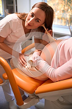 Friendly doctor examines pregnant woman listening to baby& x27;s heartbeat