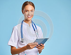 Friendly doctor nurse with tablet wireless computer smiles in isolated against ablue background