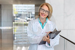 Friendly doctor physician lifestyle portrait, smiling at medical hospital workplace while writing on clipboard