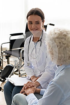 Friendly doctor supporting disabled patient during visit, holding hand