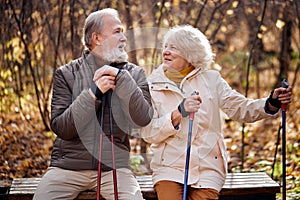 Friendly elderly couple in love engaged in Nordic walking in park, have rest