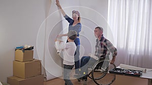 Friendly family, beloved disabled father in wheelchair with caring wife and wonderful child chooses wallpaper in new