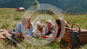 Friendly family enjoy picnic on grass mountain hill. Happy people lying blanket.