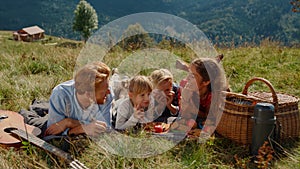 Friendly family enjoy picnic on grass mountain hill. Happy people lying blanket.