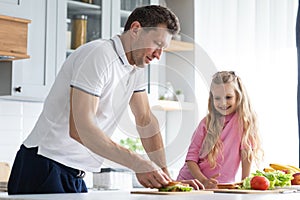 A friendly family from father with daughter stand and manage in the kitchen. A young serious man dad gives his child