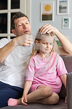 A friendly family from young father and little daughter sit near on the sofa in the room. A caring dad decorates his