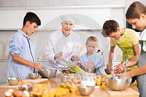 Friendly female chef in white uniform giving culinary lesson to tweens photo