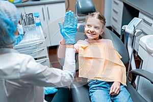 Friendly female dentist giving high five little girl sitting on stomatological chair after treatment