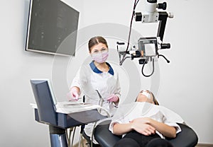 Friendly female dentist with patient during dental procedure with microscope in dental office