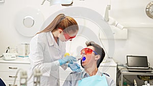 Friendly female dentist talking with smiling male patient speaking after composite dental filling