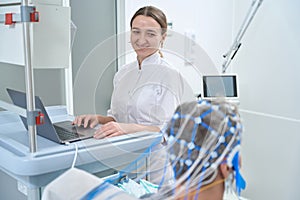 Friendly female diagnostician performs EEG - electroencephalography in clinic