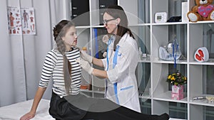 Friendly female doctor examining a girl teenager in the room in the hospital. The doctor listens to the breathing and