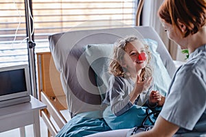 Friendly female doctor examining small girl in bed in hospital.