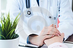 Friendly female doctor hands holding patient hand sitting at the desk for encouragement, empathy, cheering and support