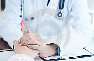 Friendly female doctor hands holding patient hand sitting at the desk for encouragement, empathy, cheering and support