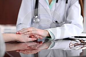 Friendly female doctor hands holding patient hand sitting at the desk for encouragement, empathy, cheering and support