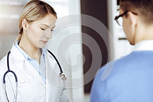 Friendly female doctor and patient man discussing current health examination while sitting in sunny clinic. Perfect