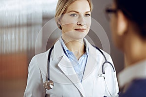 Friendly female doctor and patient man discussing current health examination while sitting in sunny clinic. Perfect