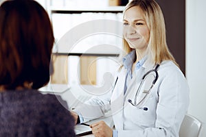 Friendly female doctor and patient woman discussing current health examination while sitting in sunny clinic. Perfect