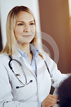 Friendly female doctor and patient woman discussing current health examination while sitting in sunny clinic. Perfect