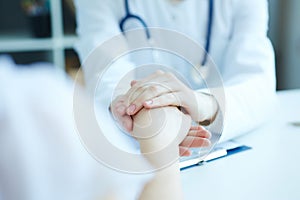 Friendly female doctor`s hands holding female patient`s hand for encouragement and empathy.