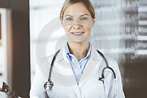Friendly female doctor standing and holding clipboard in clinic . Portrait of cheerful smiling physician. Perfect