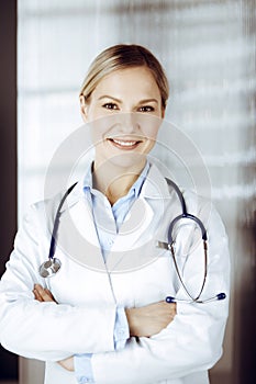 Friendly female doctor standing in sunny clinic. Portrait of cheerful smiling physician. Perfect medical service in