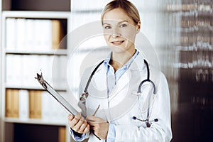 Friendly female doctor standing in sunny clinic. Portrait of cheerful smiling physician. Perfect medical service in