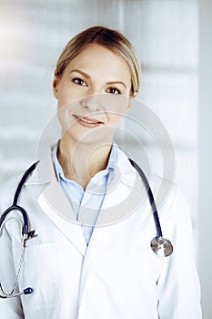 Friendly female doctor standing in sunny clinic. Portrait of cheerful smiling physician. Perfect medical service in