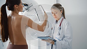Friendly Female Doctor with Tablet Computer Explains Mammogram Procedure to a Topless Adult Female