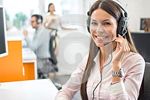 Friendly female helpline operator with headphones in call center