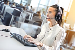 Friendly female helpline operator working on her workspace at large busy call center office