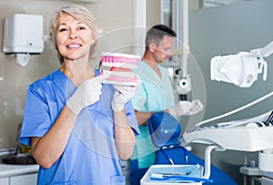 Friendly female stomatologist demonstrating tooth brushing on jaw model