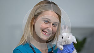 Friendly female vet holding cute rabbit, advertisement of veterinary clinic