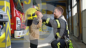 Friendly firefighter puts a protective helmet to a little boy