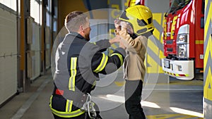 Friendly firefighter puts a protective helmet to a little boy