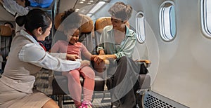 Friendly flight attendant take car kid passenger on board. Cabin crew helping curly African girl to faster her seat belt